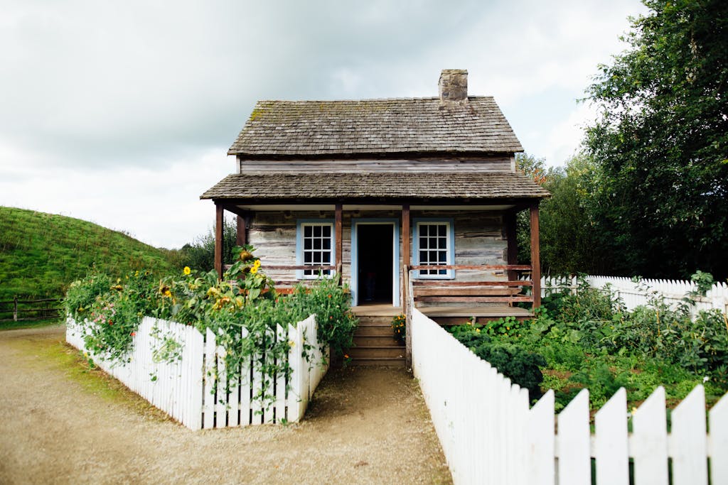 A quaint wooden cabin surrounded by greenery and a white picket fence, embodying rustic charm.